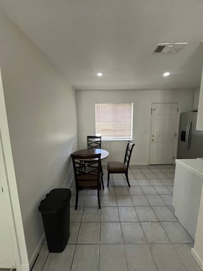 A compact kitchen with a dining area, a window with blinds, and a door leading to another room. - Spacious 1BR Apt, gated parking-near downtown (Sacramento)