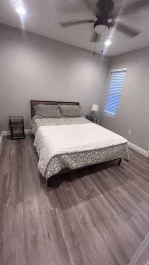 A bedroom with a bed, a nightstand, a lamp, a ceiling fan, and a window with blinds. - Spacious 1BR Apt, gated parking-near downtown (Sacramento)