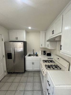 A compact kitchen with white cabinets, a stainless steel refrigerator, a gas stove, and a sink.