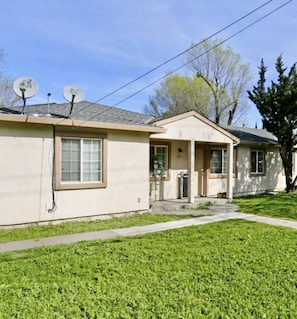 A single-story house with a front porch, satellite dishes, and a well-maintained lawn. - Spacious 1BR Apt, gated parking-near downtown (Sacramento)