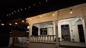 Un espace extérieur aménagé en patio, doté d’un coin salon couvert, d’un escalier menant à un niveau supérieur et d’un extincteur visible au sol.