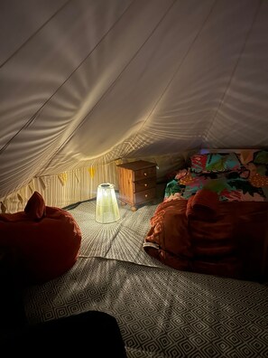 Um quarto de sótão com chão estampado, um pequeno baú de madeira, um candeeiro pendente e dois puffs.