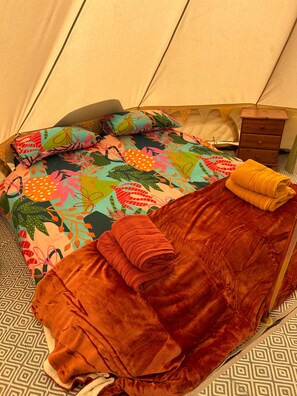 Uma tenda com cama, almofadas, uma mesa de cabeceira de madeira e uma toalha dobrada.