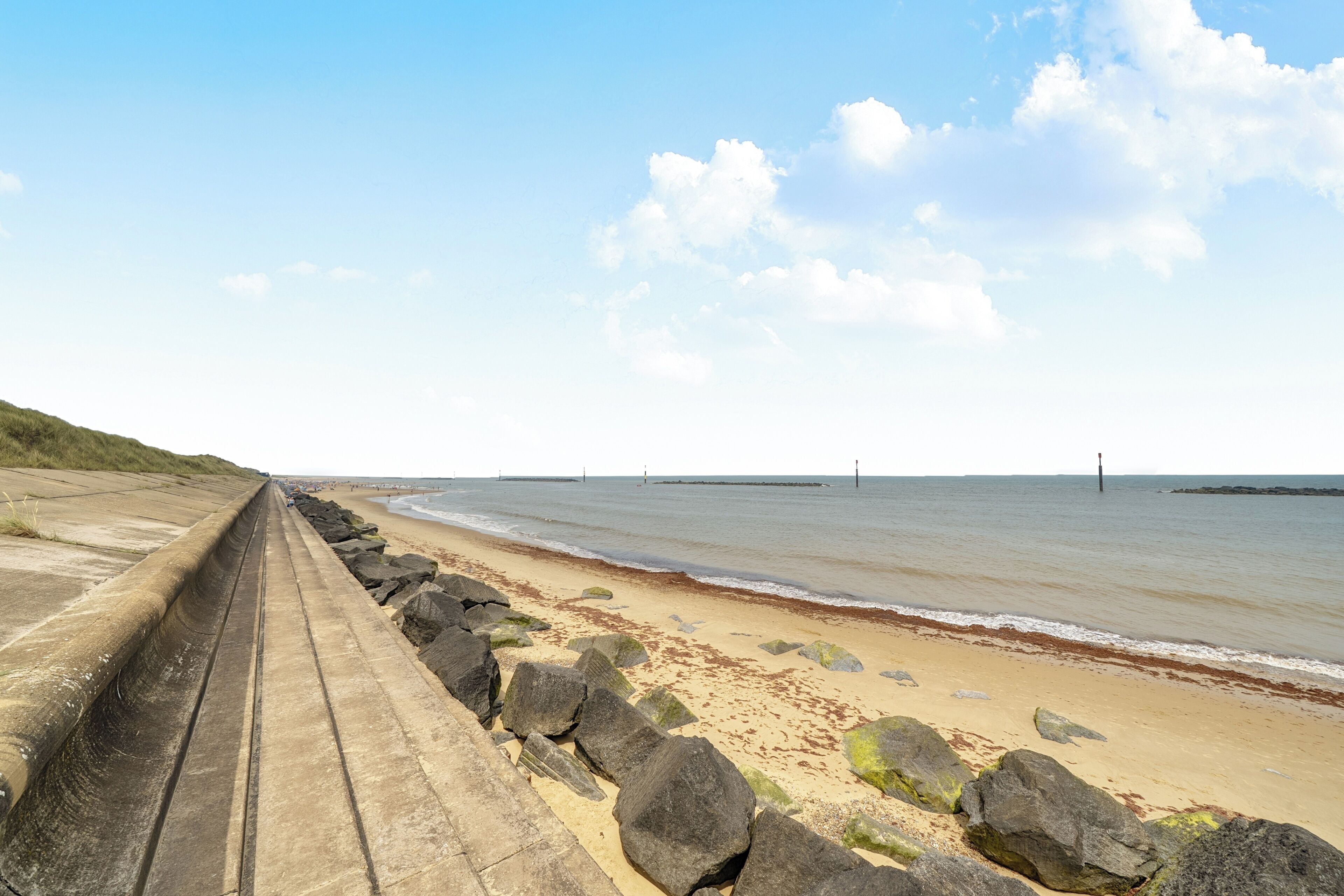 A coastal walkway with a concrete barrier, sandy beach, and rocky outcrops.