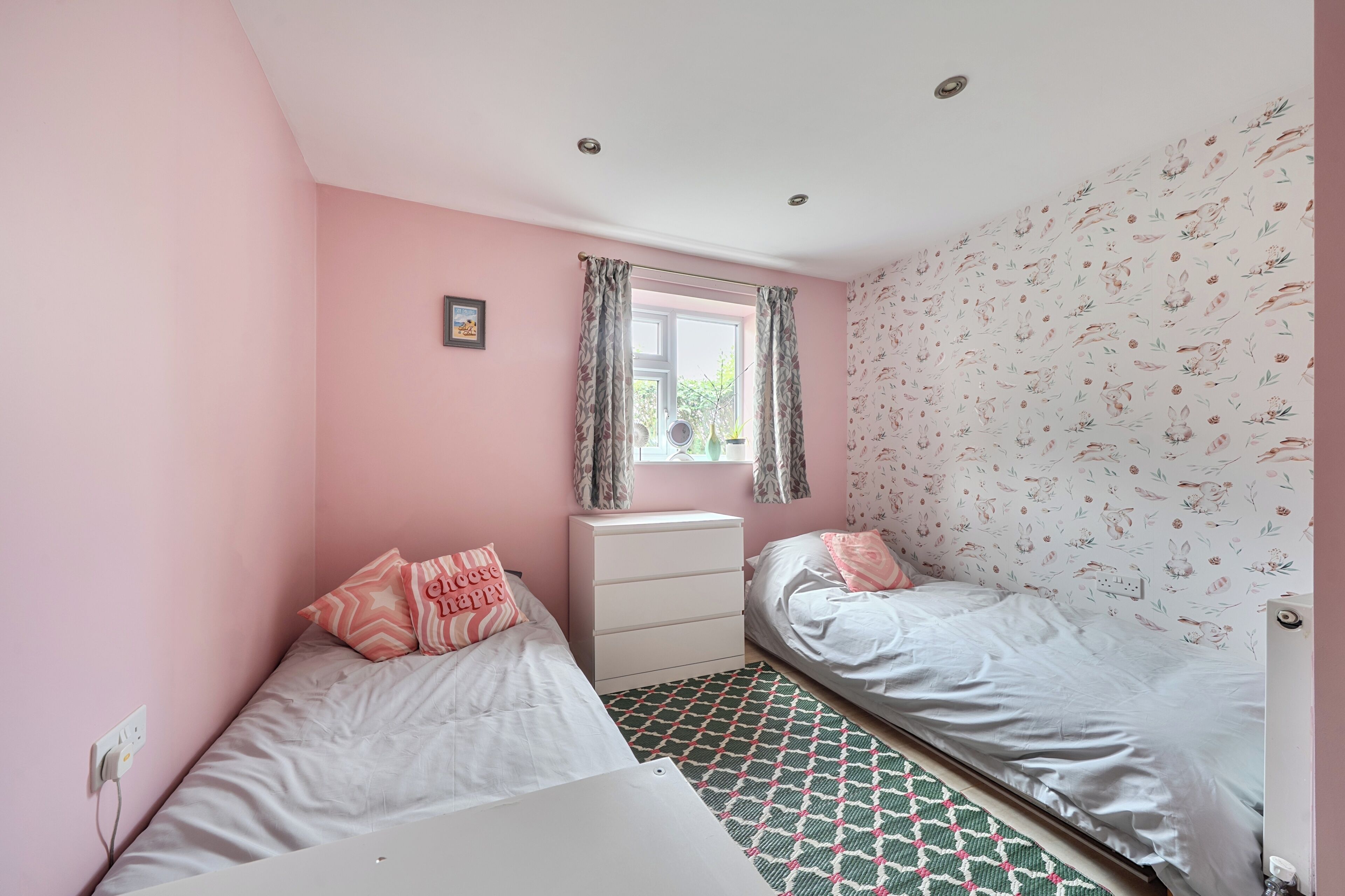 Een slaapkamer met twee bedden, een raam met gordijnen, een radiator en een muur met een bloemenmotief.