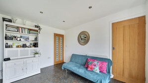 A living room with a blue sofa, a white cabinet, and a wooden door. - Sea Palling 2 bed /2 bath beach apartment Sleeps 4 (Norwich)