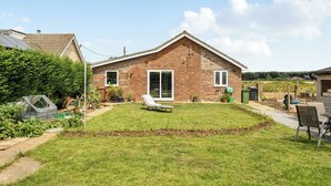 A single-story brick house with a well-maintained lawn, a patio chair, and a garden shed. - Sea Palling 2 bed /2 bath beach apartment Sleeps 4 (Norwich)