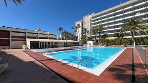 Ein Pool mit Fliesen umgeben, eine Parkgarage und ein mehrstöckiges Gebäude mit Balkonen.