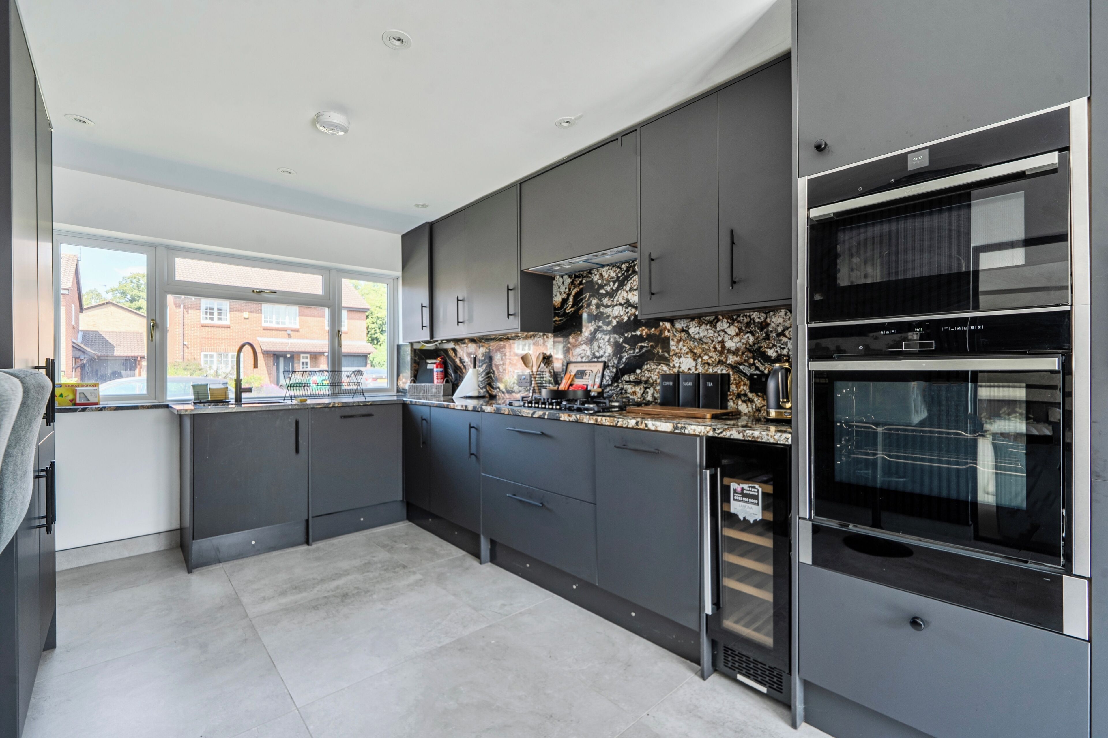 Een moderne keuken met donkere kastjes, een groot raam en een ingebouwde oven.