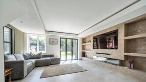 Un salon moderne avec un canapé d’angle gris, une cheminée et un téléviseur fixé sur un mur en pierre.