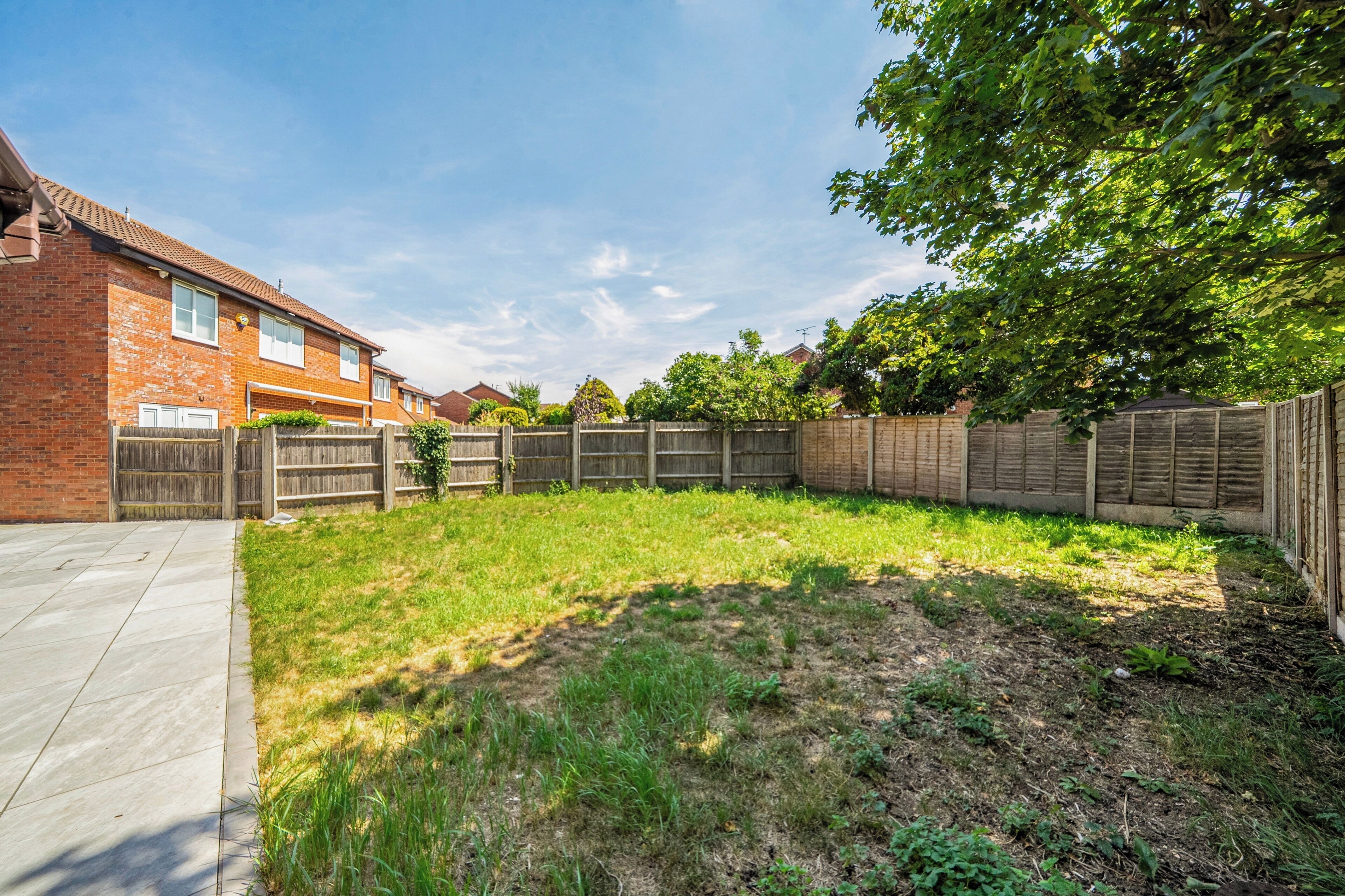 A residential backyard with a paved patio, a wooden fence, and a grassy area.