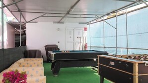 Een pooltafel, een tafelvoetbalspel en een bank in een ruimte met een groen tapijt en metalen steigers.