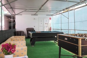 Ein Billardtisch, ein Kicker und eine Couch in einem Raum mit grünem Teppich und Metallgerüsten.