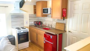 A compact kitchen with a stove, microwave, sink, and a red refrigerator. - Brewery Lodge Sleeps 4 (Lydney)