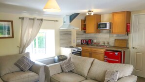 A living room with a sofa and a coffee table, a kitchen with wooden cabinets and appliances, and a window with curtains. - Brewery Lodge Sleeps 4 (Lydney)