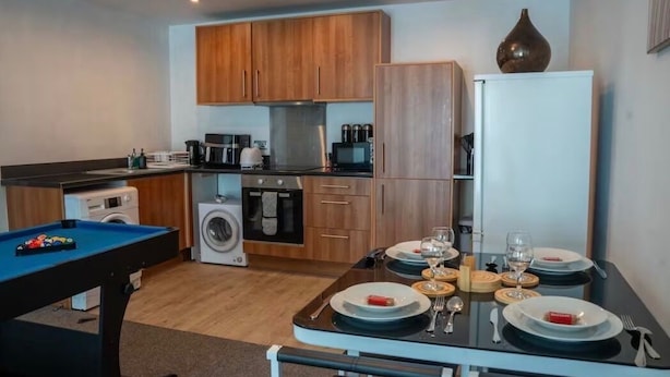 Una cocina compacta con armarios de madera, lavadora, una mesa de comedor para cuatro personas y una mesa de billar.