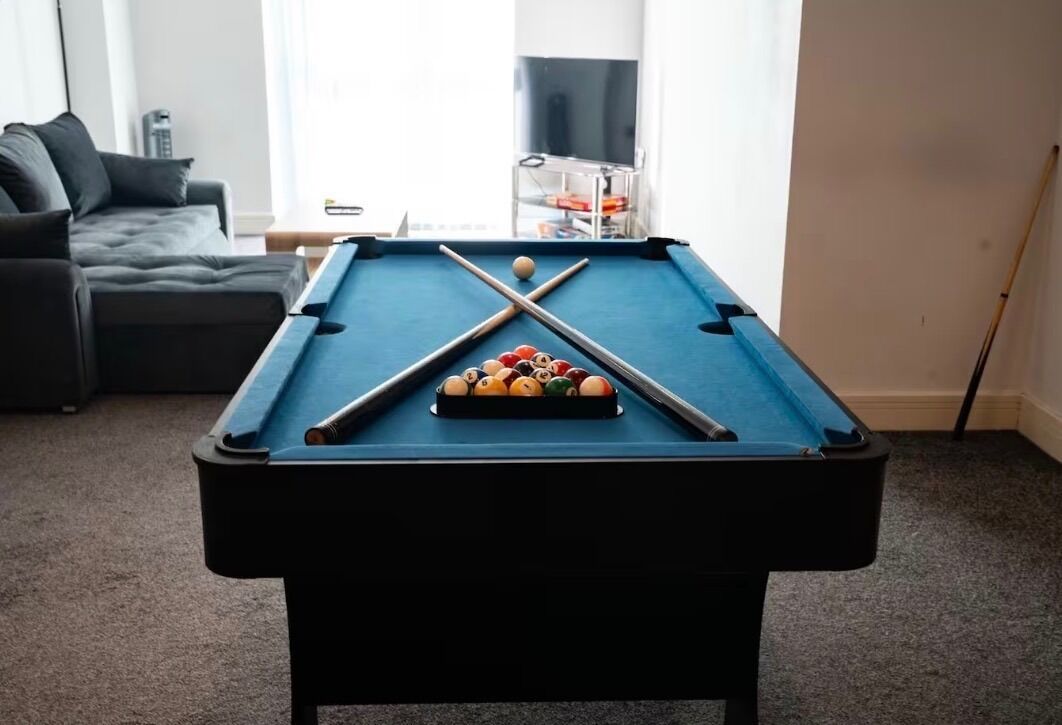A pool table in a living room with a sofa and a TV in the background.