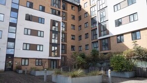 Un edificio residencial de varios pisos con un diseño arquitectónico moderno, con balcones, ventanas amplias y un patio ajardinado con jardineras.