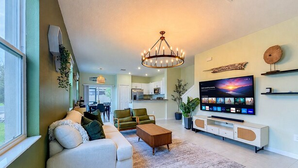 A living room with a sofa, coffee table, TV, and a chandelier. - Designer Home with Community Pool Near Apollo Beach (Ruskin)