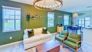 A living room with a white sofa, green armchairs, a wooden coffee table, a chandelier, and hexagonal wall decorations. - Designer Home with Community Pool Near Apollo Beach (Ruskin)