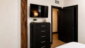 A bedroom with a bed, a dresser, a TV, and a door. - Brick & Bed - Two Bedroom Riverfront Loft (St. Louis)