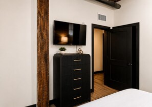 A bedroom with a bed, a dresser, a TV, and a door. - Brick & Bed - Two Bedroom Riverfront Loft (St. Louis)