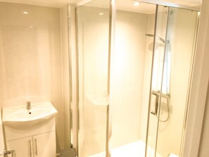 A glass-enclosed shower with a handheld showerhead, a white sink, and a cabinet below. - Apartment Sleeps 4 with Parking (Lydney)