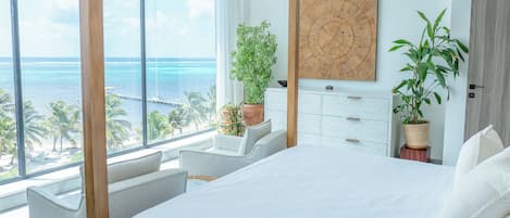 Un dormitorio con una cama grande, vista al océano y varias plantas en macetas.