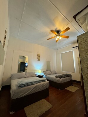 A bedroom with two beds, a ceiling fan, a TV, and a stone accent wall. - Cozy 1-bedroom 2 bathroom apartment in heart of Barbados south coast. (Bridgetown)