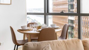 Un espace repas comprenant une table ronde, des chaises et une vue sur le paysage urbain, visible à travers de grandes fenêtres.