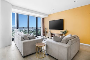 Ein modernes Wohnzimmer mit zwei Sofas, einem runden Couchtisch und einem Flachbildfernseher an der Wand.
