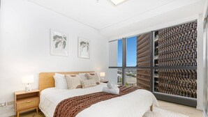 Une chambre moderne avec un grand lit, deux tables de chevet, une fenêtre avec vue et un panneau mural décoratif.
