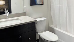 A modern bathroom with a white sink, dark cabinetry, a white toilet, and a shower curtain. - Brick & Bed - Historic Riverfront Studio (St. Louis)