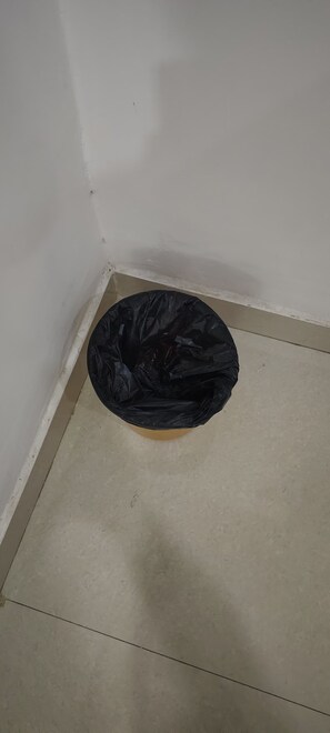 En svart sopsÀck ligger pÄ ett beige golv i ett hörn av ett rum med vita vÀggar.