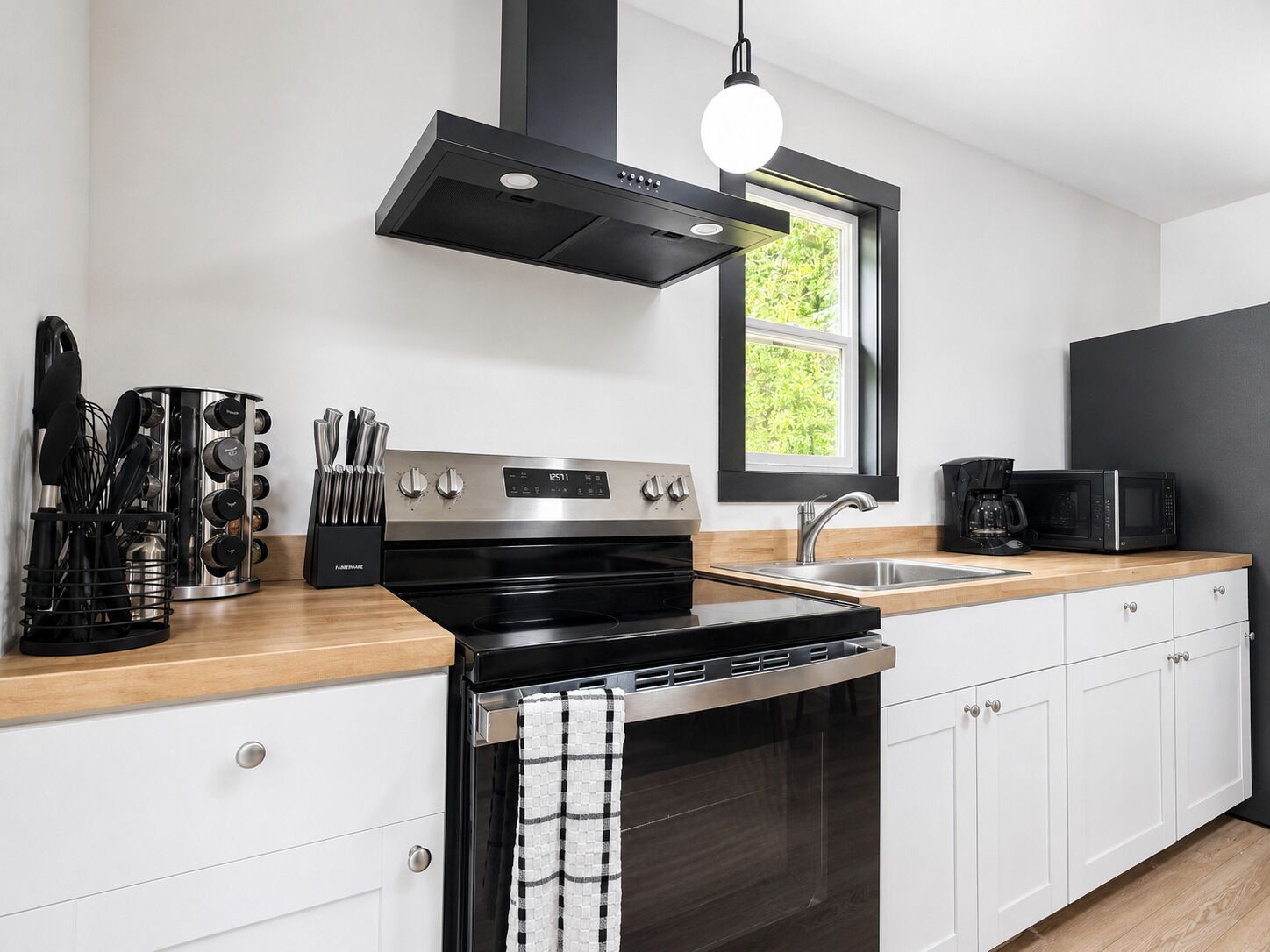 Een moderne keuken met een roestvrijstalen fornuis, een zwarte afzuigkap, een raam met uitzicht en een koffiezetapparaat op het aanrecht.