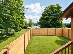 Ein umzäunter Garten mit Rasen, Bäumen und Blick auf einen See.