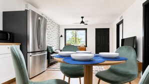A modern kitchen with a stainless steel refrigerator, a microwave, and a dining table with blue placemats and white bowls.