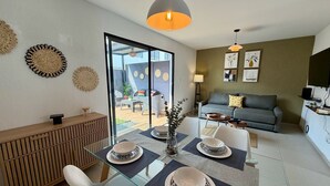 A modern living room with a glass dining table, a sofa, and a TV. - Casa Bugambilia at Senderos de Opico2 | WiFi, Pool, Gym (San Juan Opico)