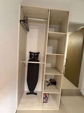 Ein begehbarer Kleiderschrank mit Bügelbrett, Regalen und einer Tür.