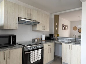 Une cuisine moderne avec des meubles en bois, une cuisinière en acier inoxydable, un four à micro-ondes et des plans de travail en granit.