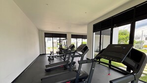 A modern gym with treadmills, weight machines, and a large window providing a view of the outdoors. - Casa Bugambilia at Senderos de Opico2 | WiFi, Pool, Gym (San Juan Opico)