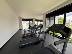 Une salle de sport moderne équipée de tapis de course, d’appareils de musculation et dotée d’une grande fenêtre offrant une vue sur l’extérieur.