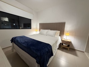 Une chambre d’hôtel avec un lit, deux lampes de chevet, une fenêtre et une tête de lit fixée au mur.