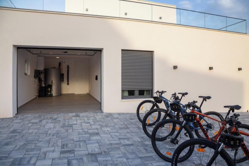 A modern building with a garage door, bicycles parked outside, and a paved entrance area.