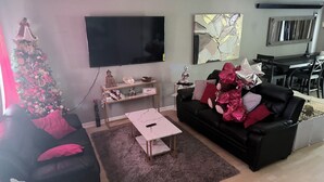 A living room with a black sofa, a coffee table, a TV, a Christmas tree, and a dining area in the background. - 2-bedroom townhome in terrific Attleboro  close to Gillette and Foxwoods (Attleboro)