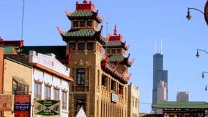 Un edificio tradicional de varios niveles y tejados rojos, con un rascacielos moderno al fondo, y una calle con varios letreros.