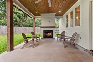 An outdoor patio with a fireplace, wooden chairs, and a concrete floor.