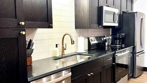 A modern kitchen with dark wood cabinets, stainless steel appliances, a built-in microwave, and a dishwasher. - Brick and Bed - Riverfront Loft - Walk to Arch (St. Louis)