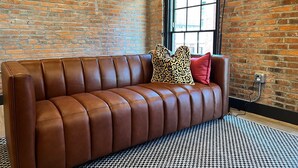 A brown leather sofa with leopard print and red pillows against a brick wall, a window, and a patterned rug. - Brick and Bed - Riverfront Loft - Walk to Arch (St. Louis)