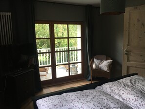 Une chambre avec un lit, une chaise, un téléviseur et une porte-fenêtre coulissante donnant sur une terrasse extérieure.